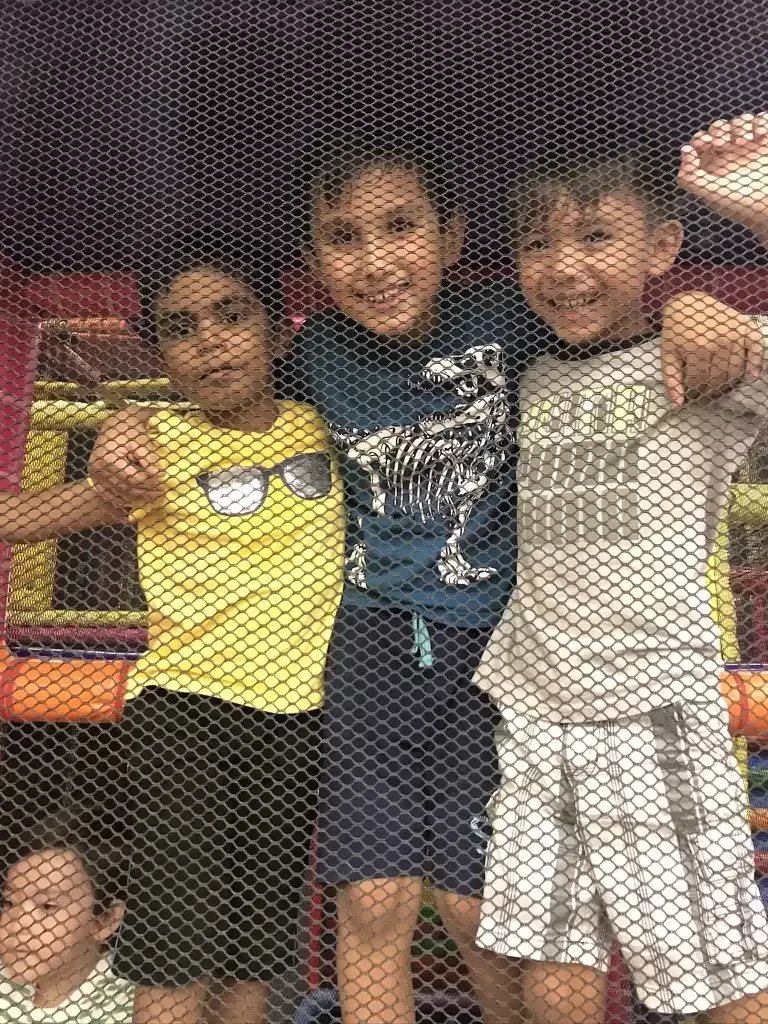 Three grinning afterschool boys pause their climb inside the indoor play structure