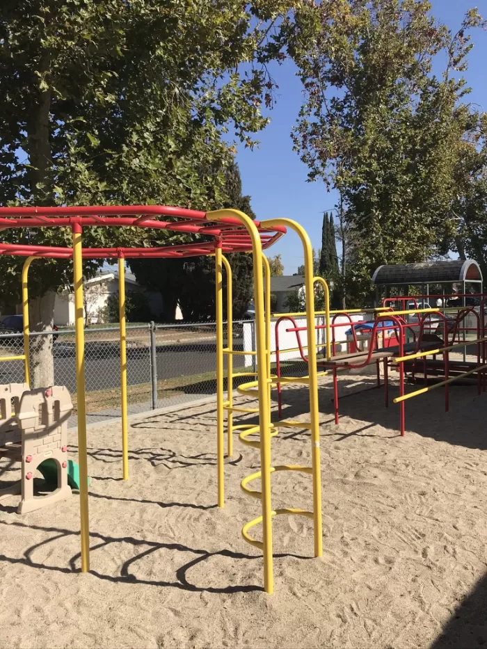 The fenced sand playground at West Hills Preschool with monkey bars and climbing structures on a sunny day